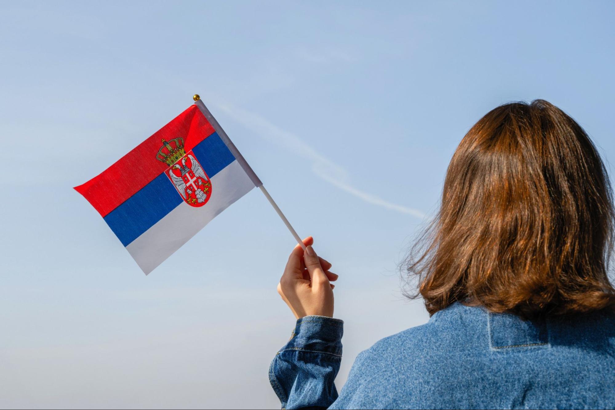 Woman hand with Serbian swaying flag on the blue sky. Serbia